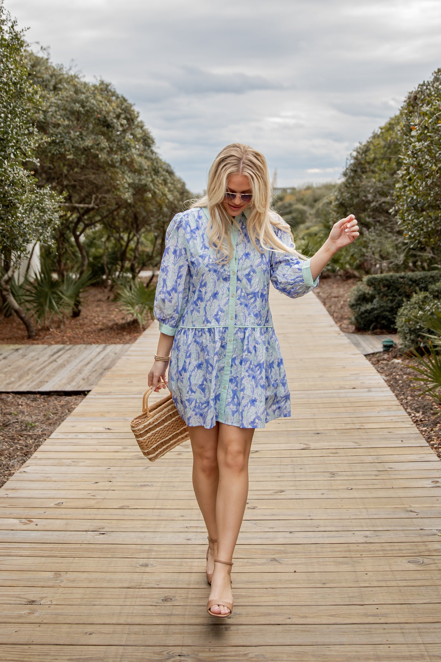 Woman in a blue floral dress walking on a wooden path with trees in the background
