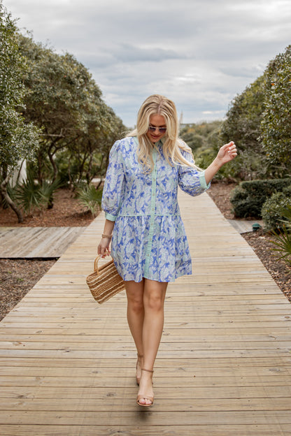 Woman in a blue floral dress walking on a wooden path with trees in the background