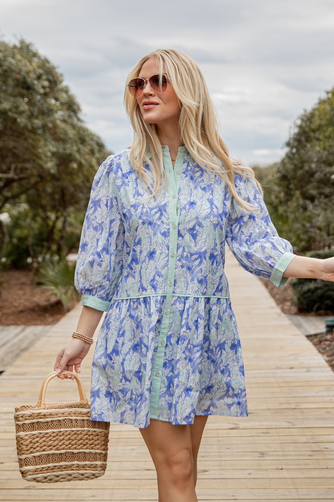 Woman in a blue floral dress standing on a wooden path with trees in the background