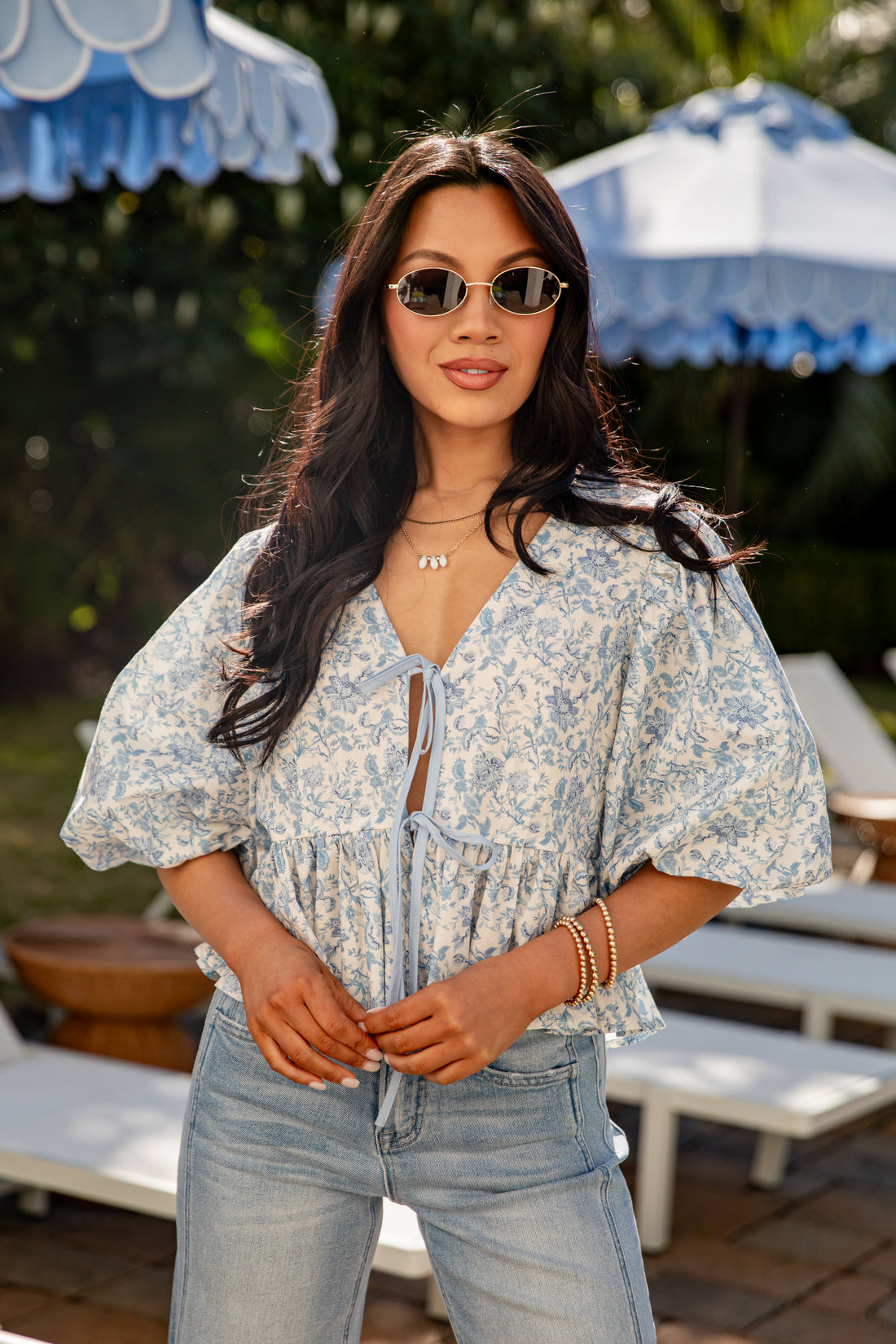 Woman wearing a floral blouse and sunglasses outdoors with umbrellas in the background