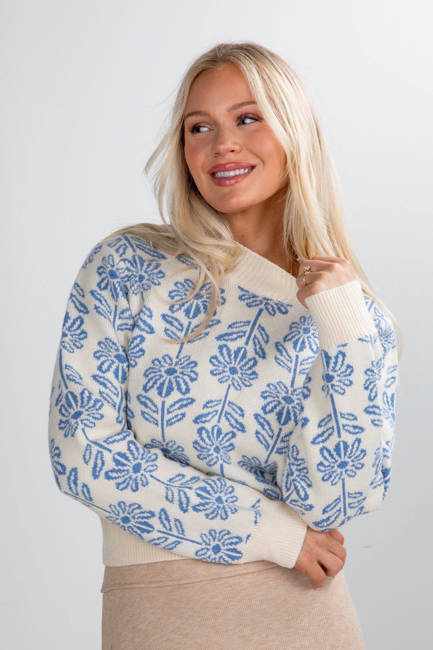 Woman wearing a cream sweater with blue floral pattern against a plain background