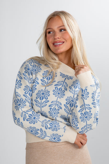 Woman wearing a cream sweater with blue floral pattern against a plain background