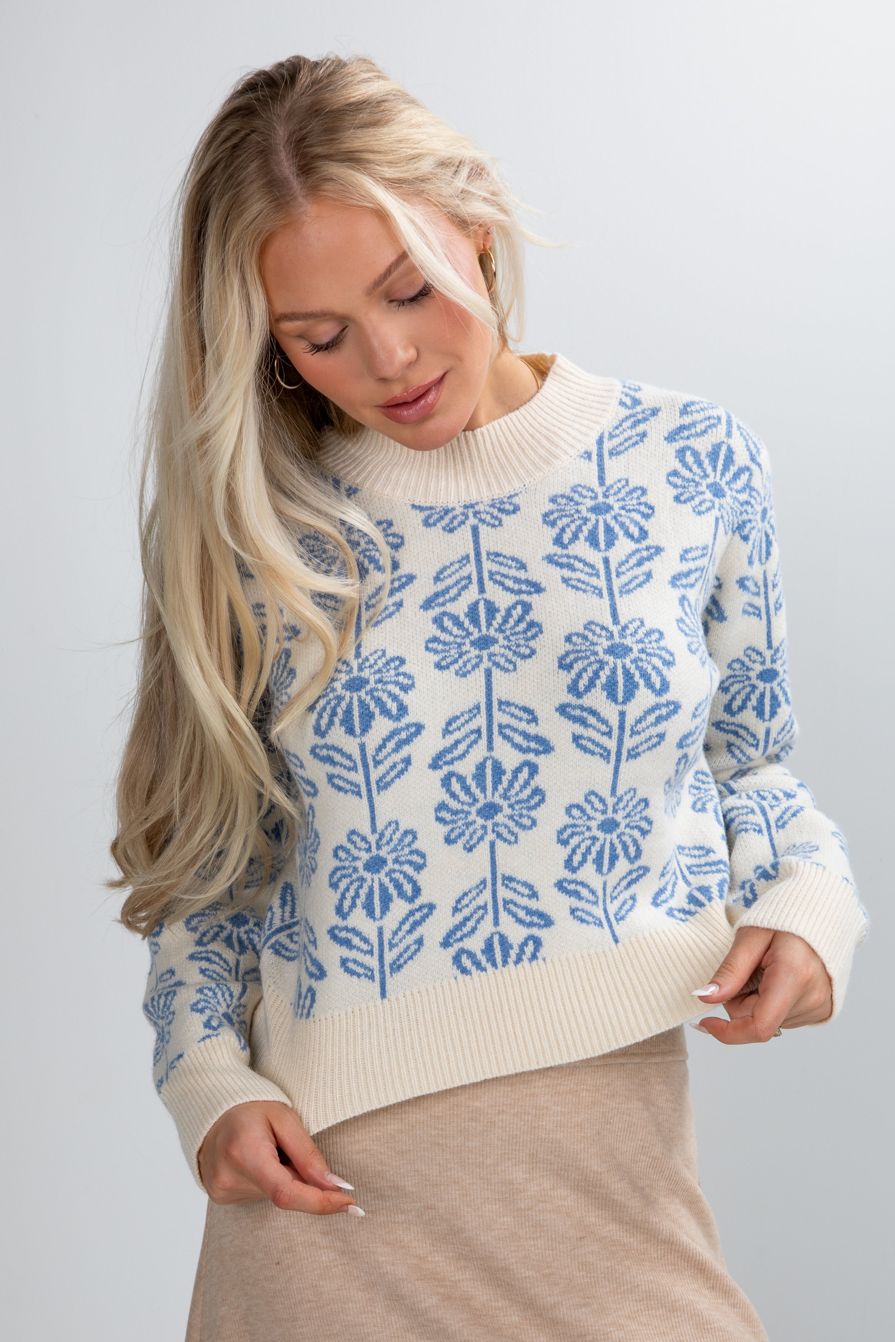 Woman wearing a white sweater with blue floral patterns on a plain background