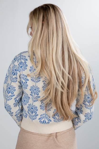 Person wearing a floral-patterned shirt with long blonde hair on a plain background