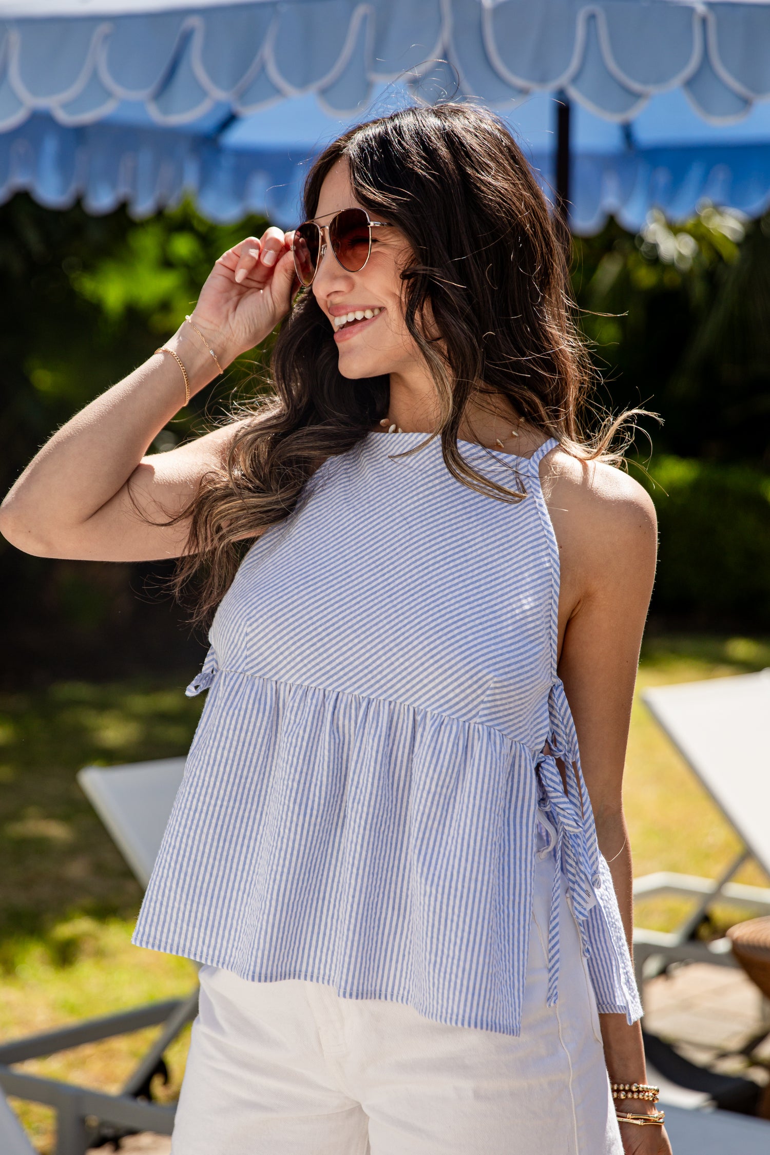 Woman wearing a blue and white striped top with sunglasses, standing outdoors.