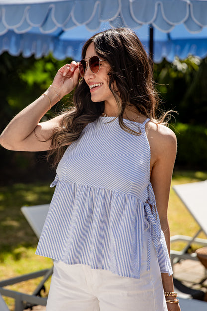Woman wearing a blue and white striped top with sunglasses, standing outdoors.