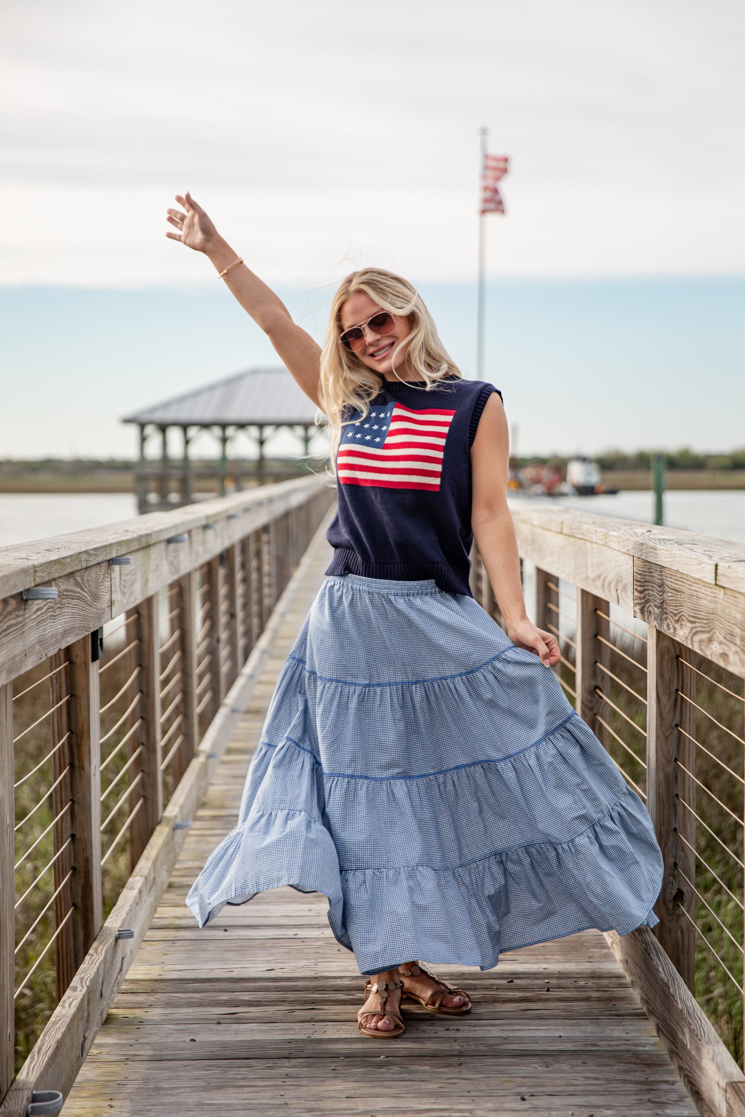 Woman on a wooden boardwalk wearing a sleeveless top with an American flag design and a long blue skirt.