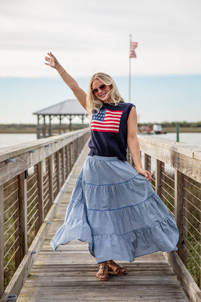 Woman on a wooden boardwalk wearing a sleeveless top with an American flag design and a long blue skirt.