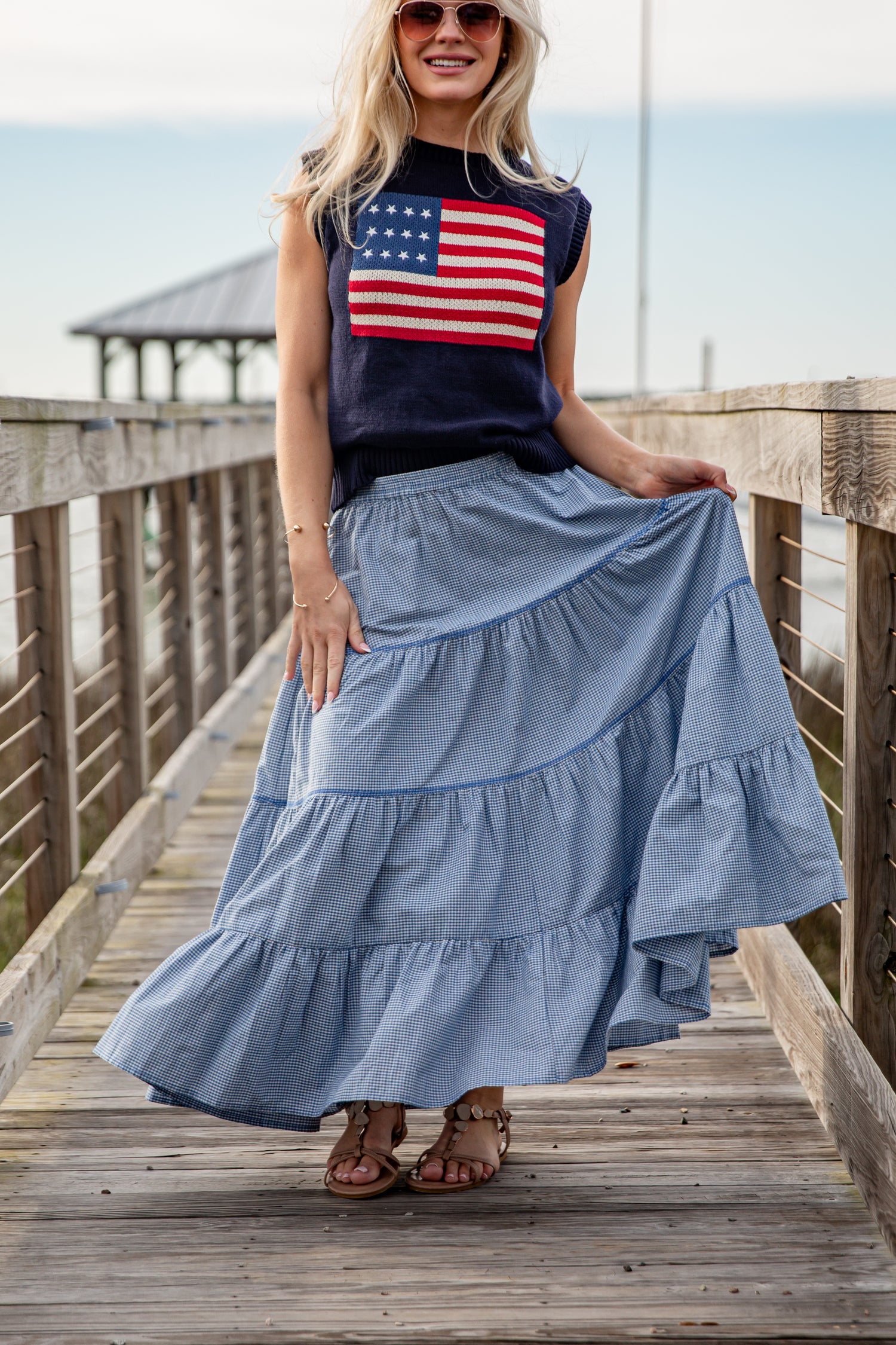 Woman wearing a sleeveless top with an American flag design and a long blue skirt on a wooden boardwalk.