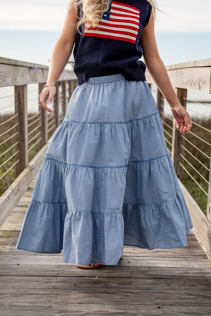 Person wearing a blue tiered skirt and American flag top on a wooden deck.