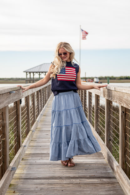 Woman standing on a wooden boardwalk wearing an American flag top and blue skirt.