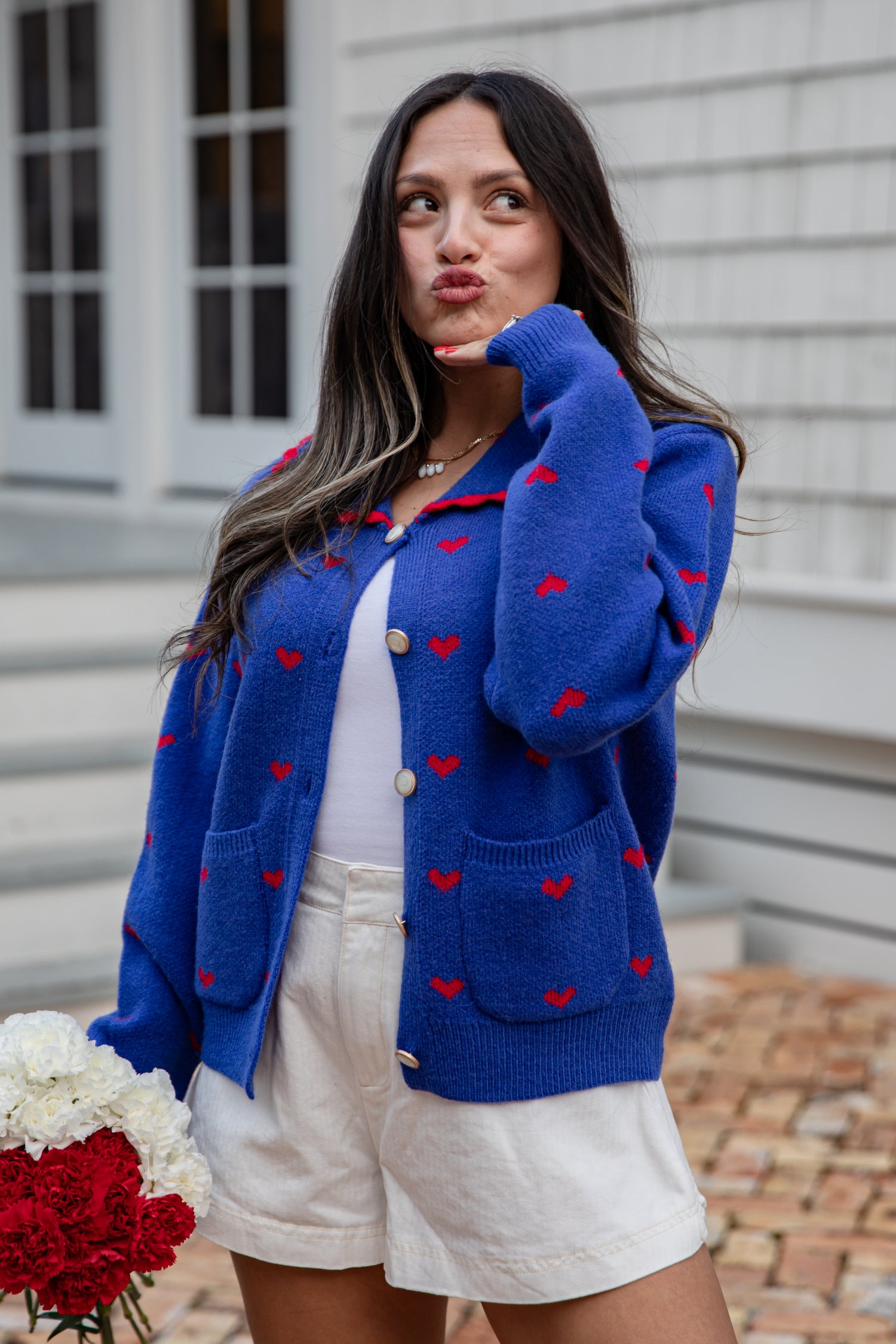 Woman wearing a blue cardigan with red heart patterns, standing outdoors.
