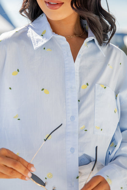 Close-up of a person wearing a light blue shirt with lemon pattern outdoors.