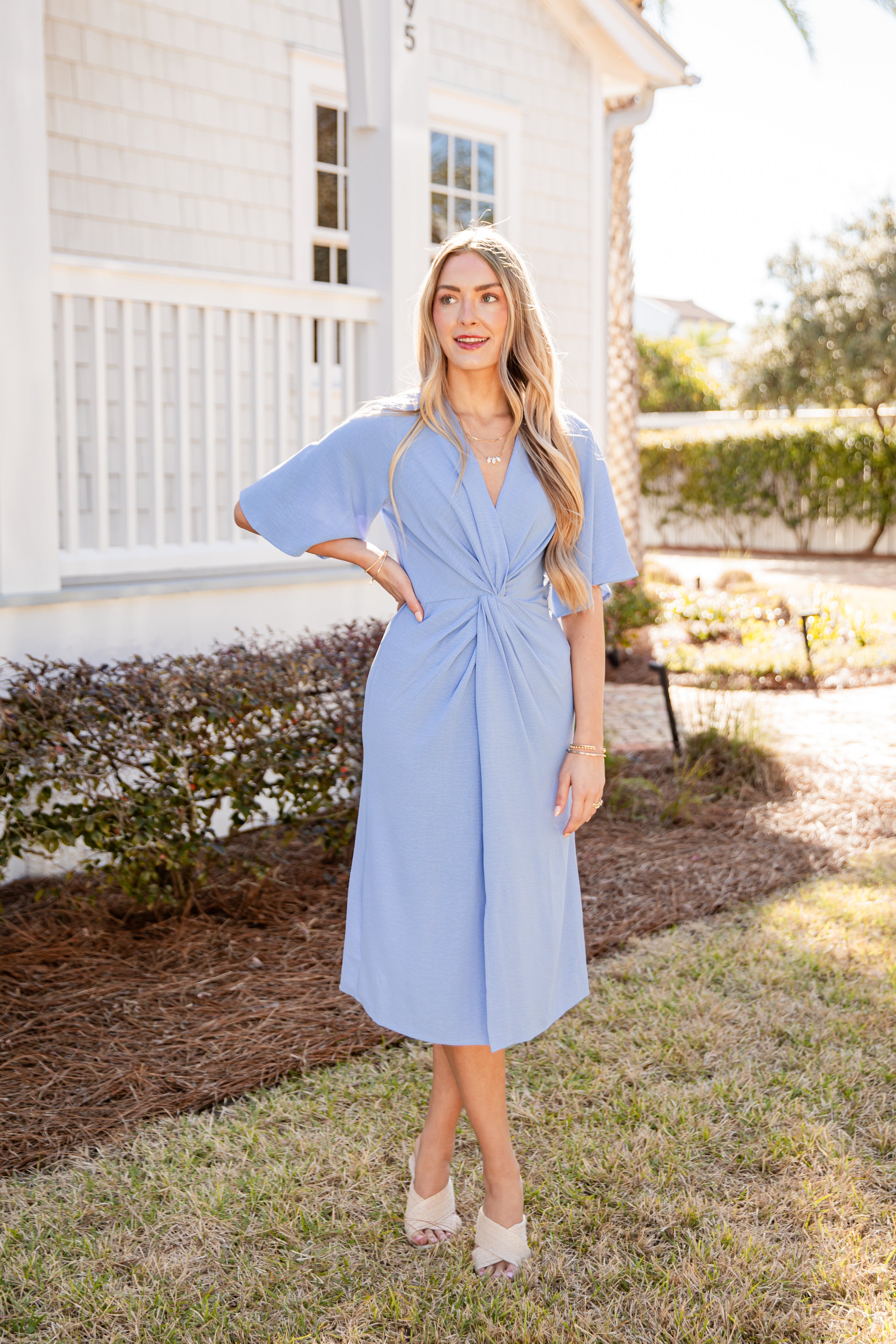 Woman in a light blue dress standing outdoors near a house.