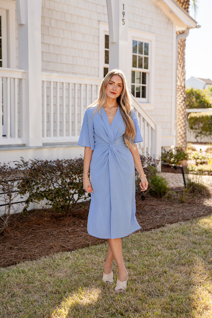 Woman in a light blue dress standing in front of a house.
