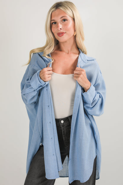 Woman wearing a light blue jacket over a white top and black pants on a plain background