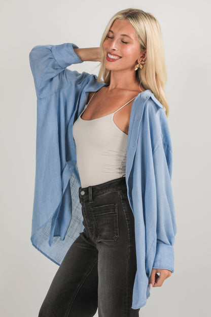 Woman wearing a light blue shirt over a beige tank top and black pants on a plain background