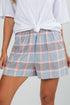 Person wearing plaid shorts with a white top on a plain background
