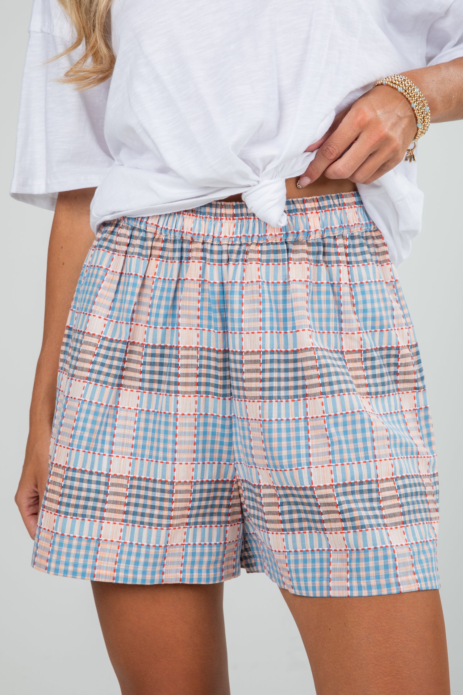Person wearing a white top and blue and pink plaid shorts on a plain background