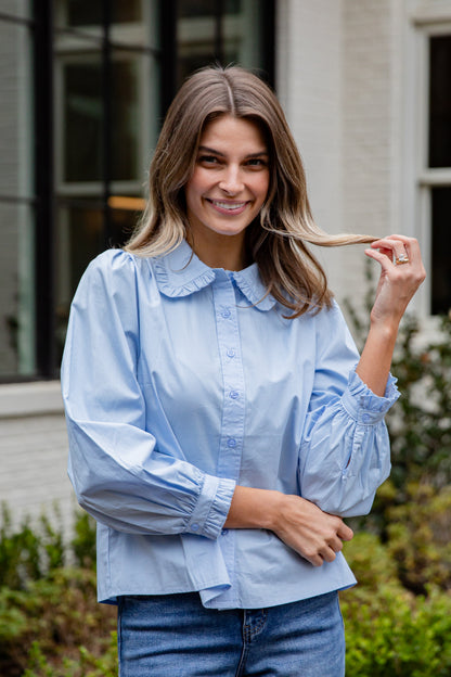Woman wearing a light blue blouse with ruffled sleeves outdoors.