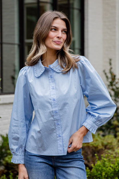 Woman wearing a light blue shirt and jeans standing outdoors.