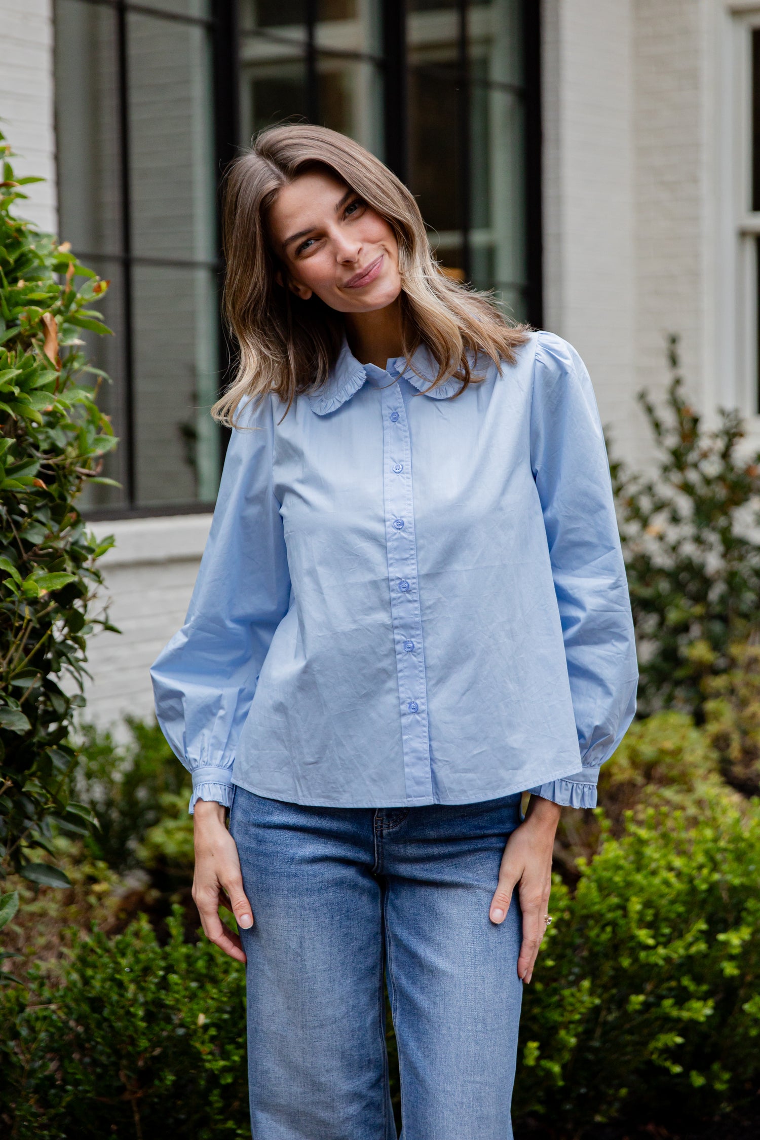 Woman wearing a light blue shirt and jeans standing outdoors.
