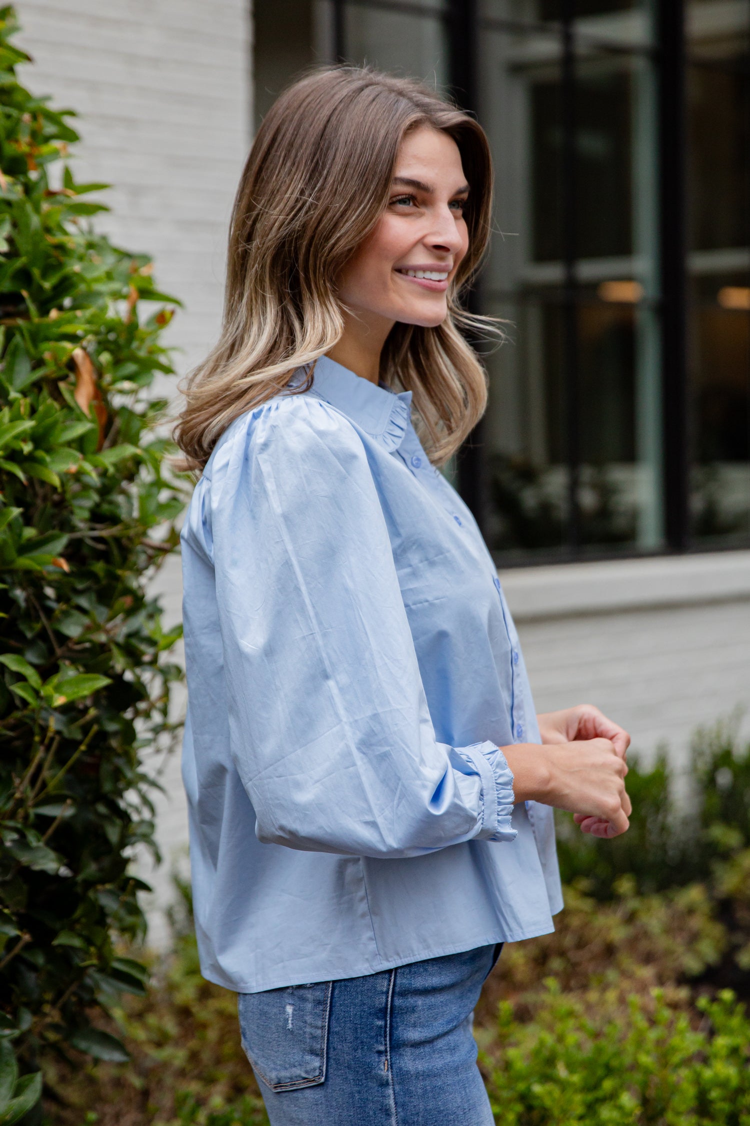 Woman wearing a light blue blouse and jeans standing outdoors.