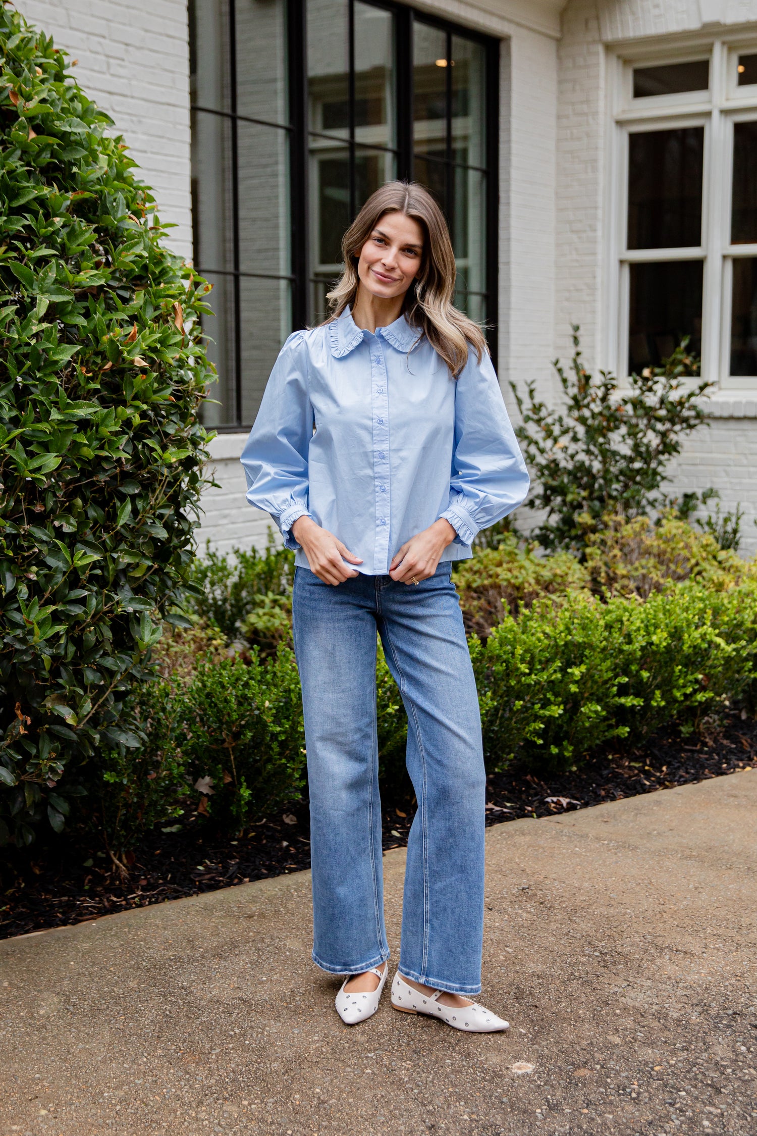 Woman wearing a light blue shirt and jeans standing outdoors.