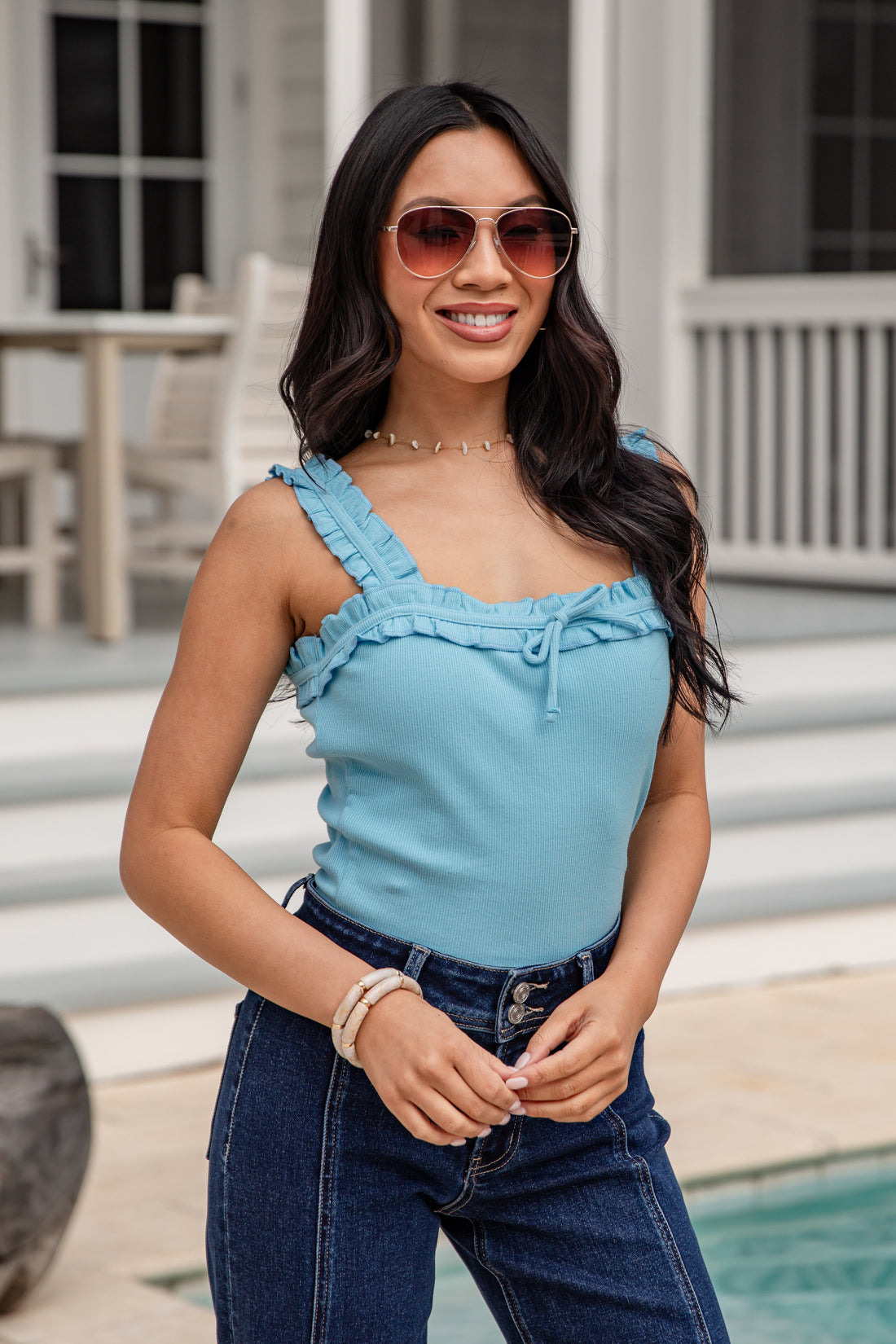 Woman wearing a blue top and sunglasses outdoors by a pool