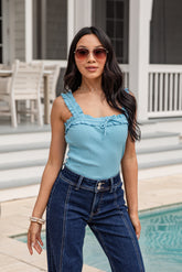Woman wearing a light blue top and dark blue jeans standing by a pool.