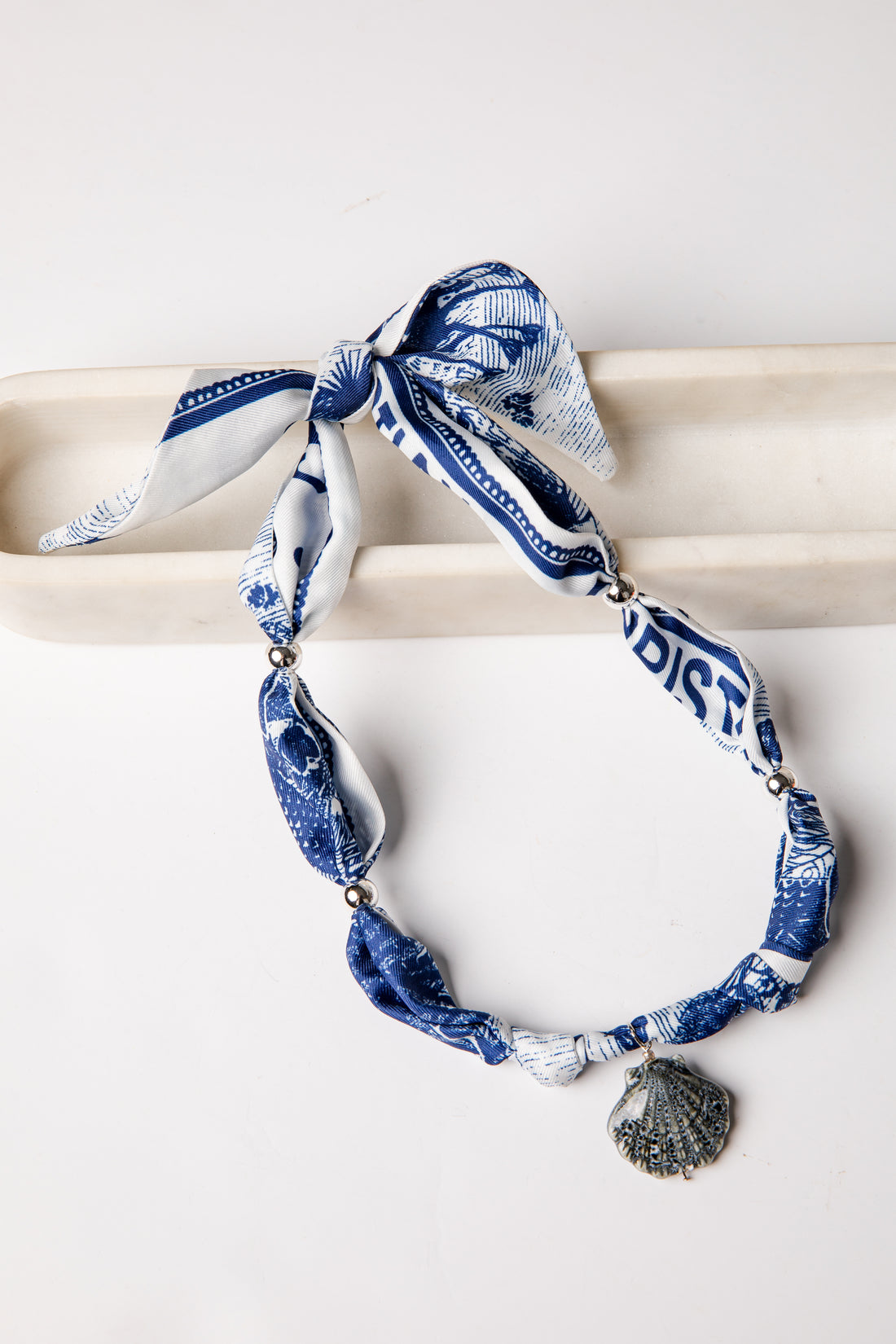 Blue and white patterned scarf with shell charm on a white background