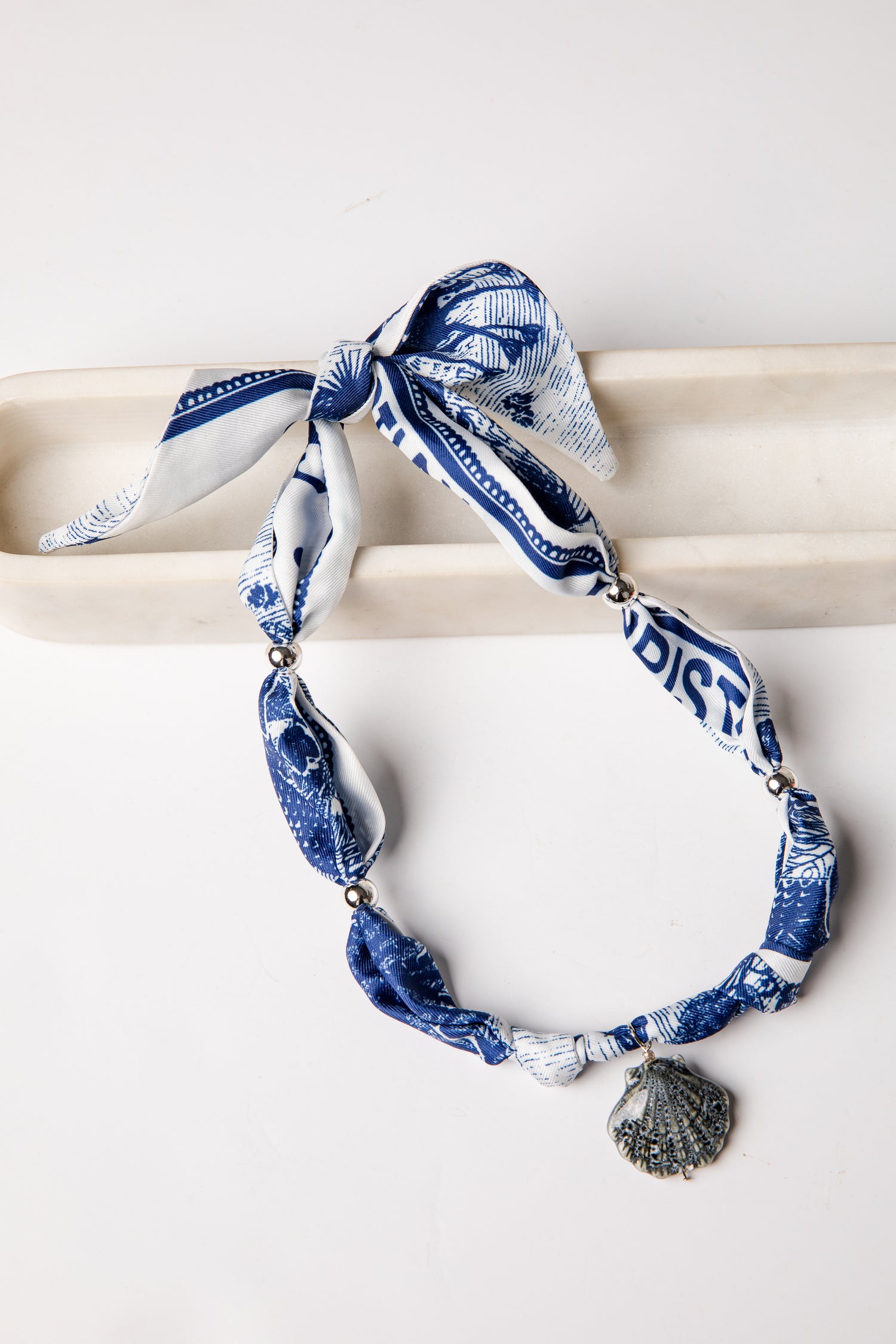 Blue and white patterned scarf with shell charm on a white background