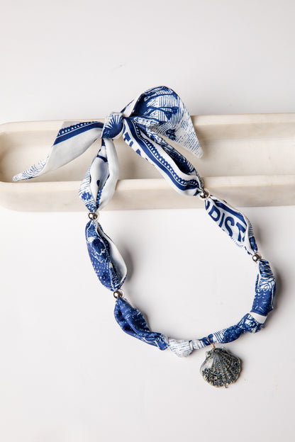 Blue and white patterned scarf with shell charm on a white background