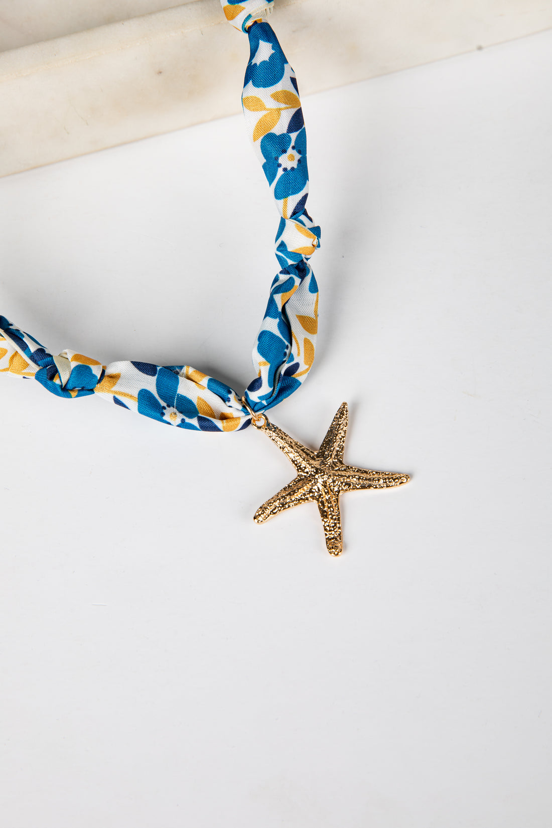 Necklace with blue and yellow floral pattern and gold starfish pendant on a white background