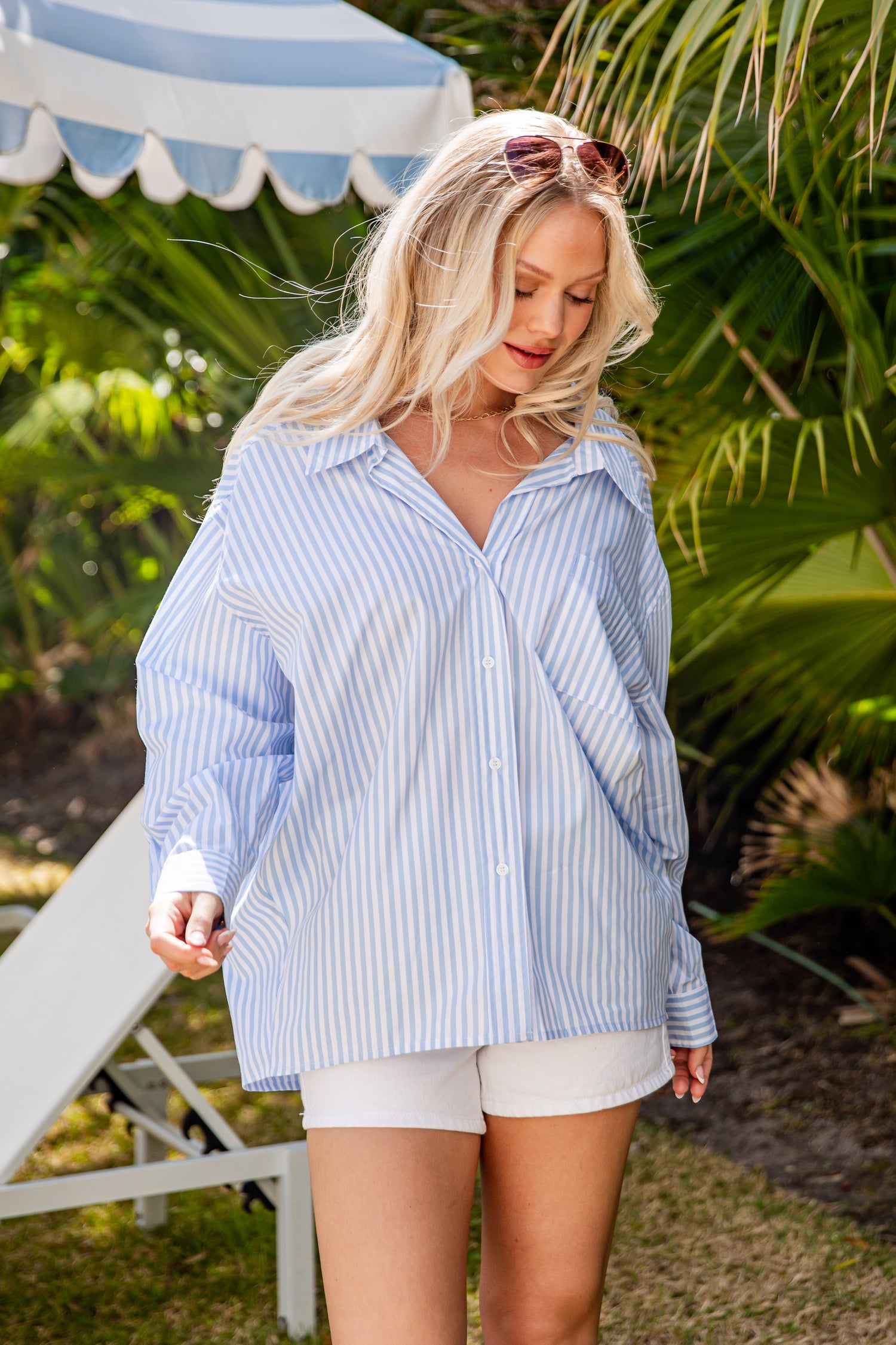 Woman wearing a blue striped shirt and white shorts outdoors with greenery in the background