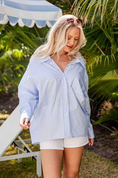 Woman wearing a blue striped shirt and white shorts outdoors with greenery in the background