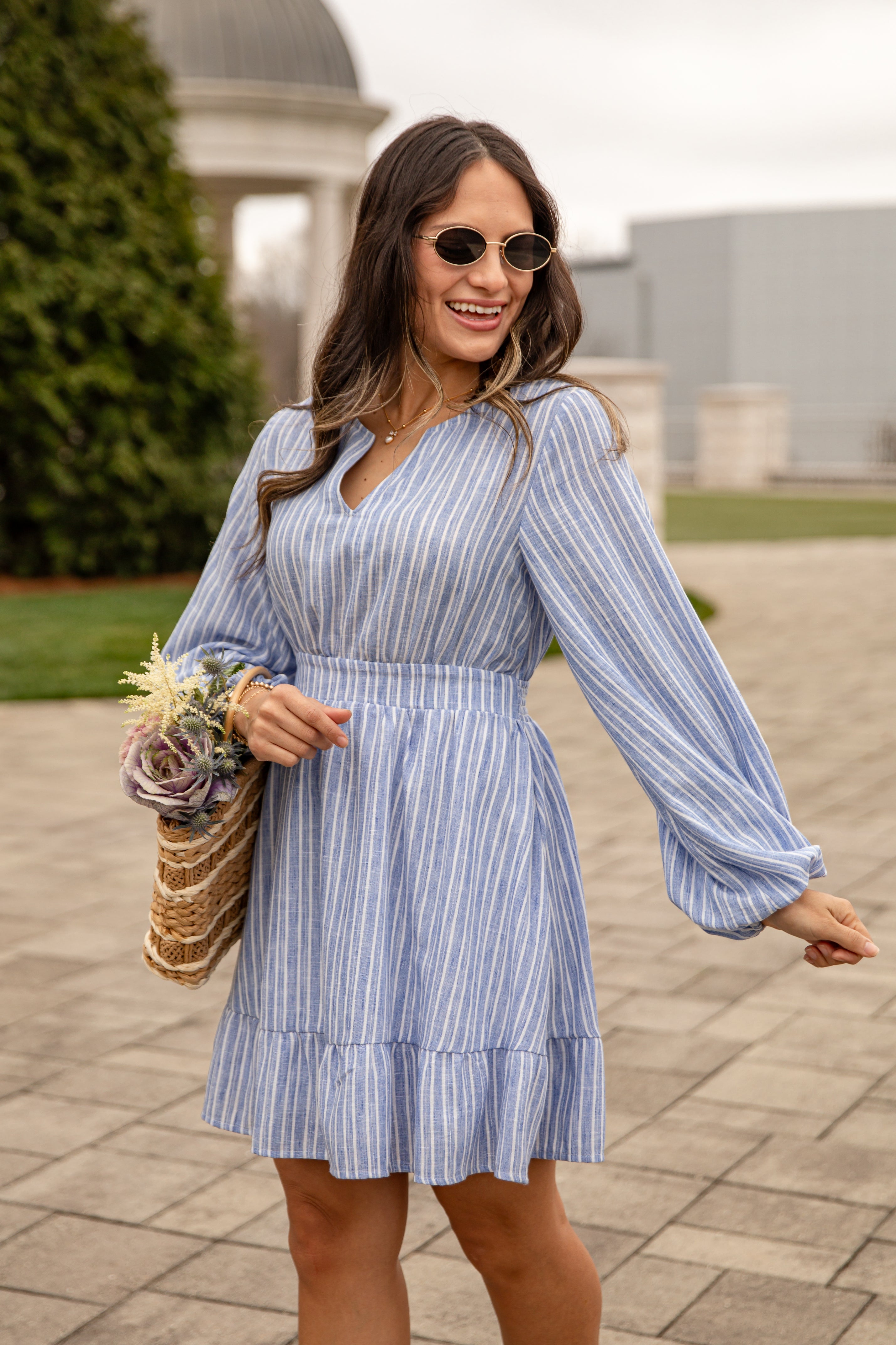 Woman in a blue striped dress holding flowers outdoors.