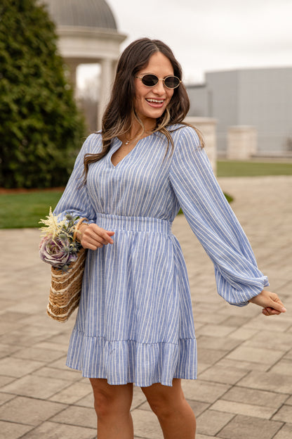 Woman in a blue striped dress holding flowers outdoors.