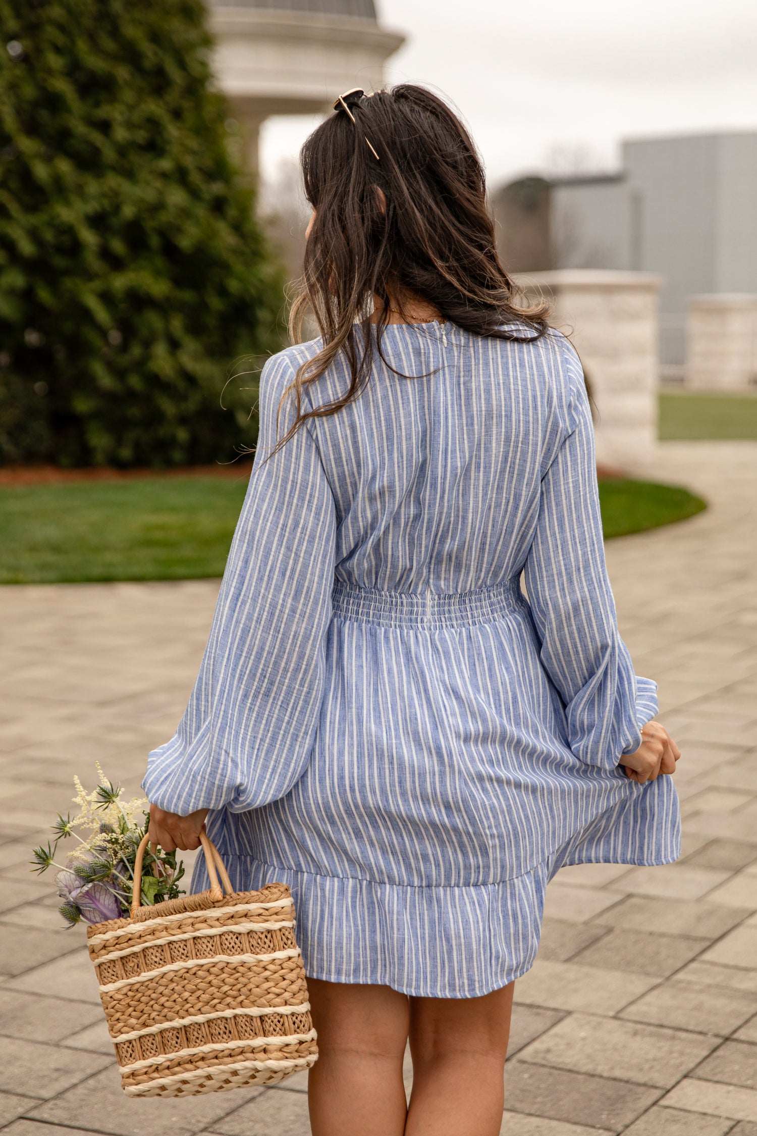 Woman in a blue striped dress holding a woven bag outdoors.