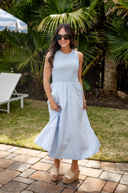 Woman in a light blue dress standing outdoors with palm trees in the background