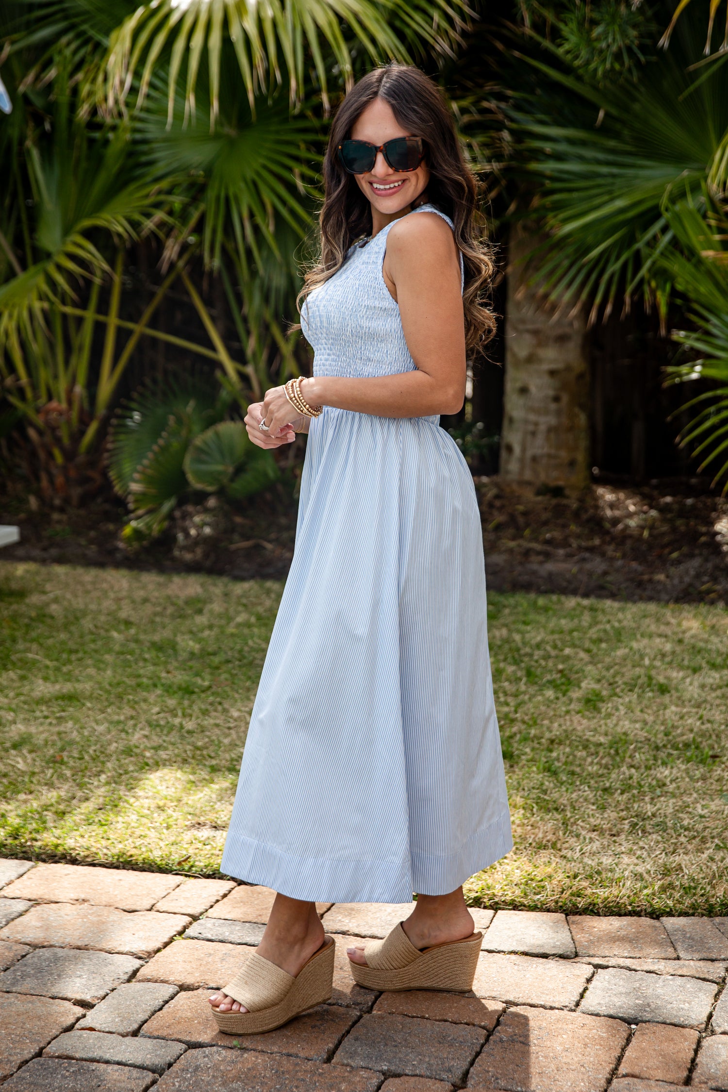 Woman in a light blue dress standing outdoors with greenery in the background