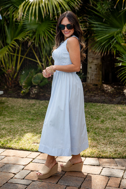 Woman in a light blue dress standing outdoors with greenery in the background