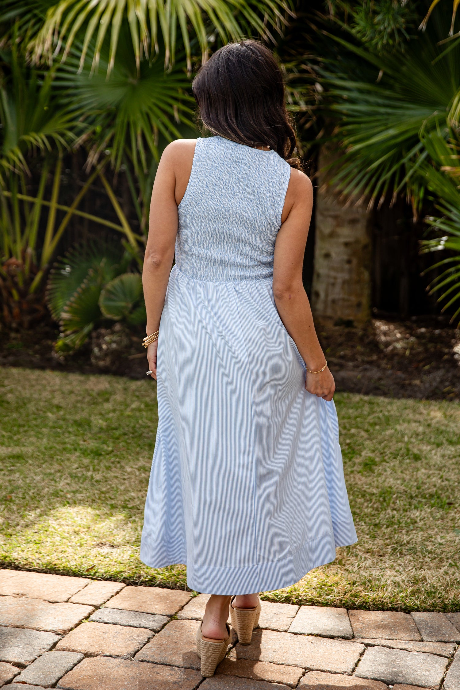 Woman in a light blue dress standing outdoors with greenery in the background