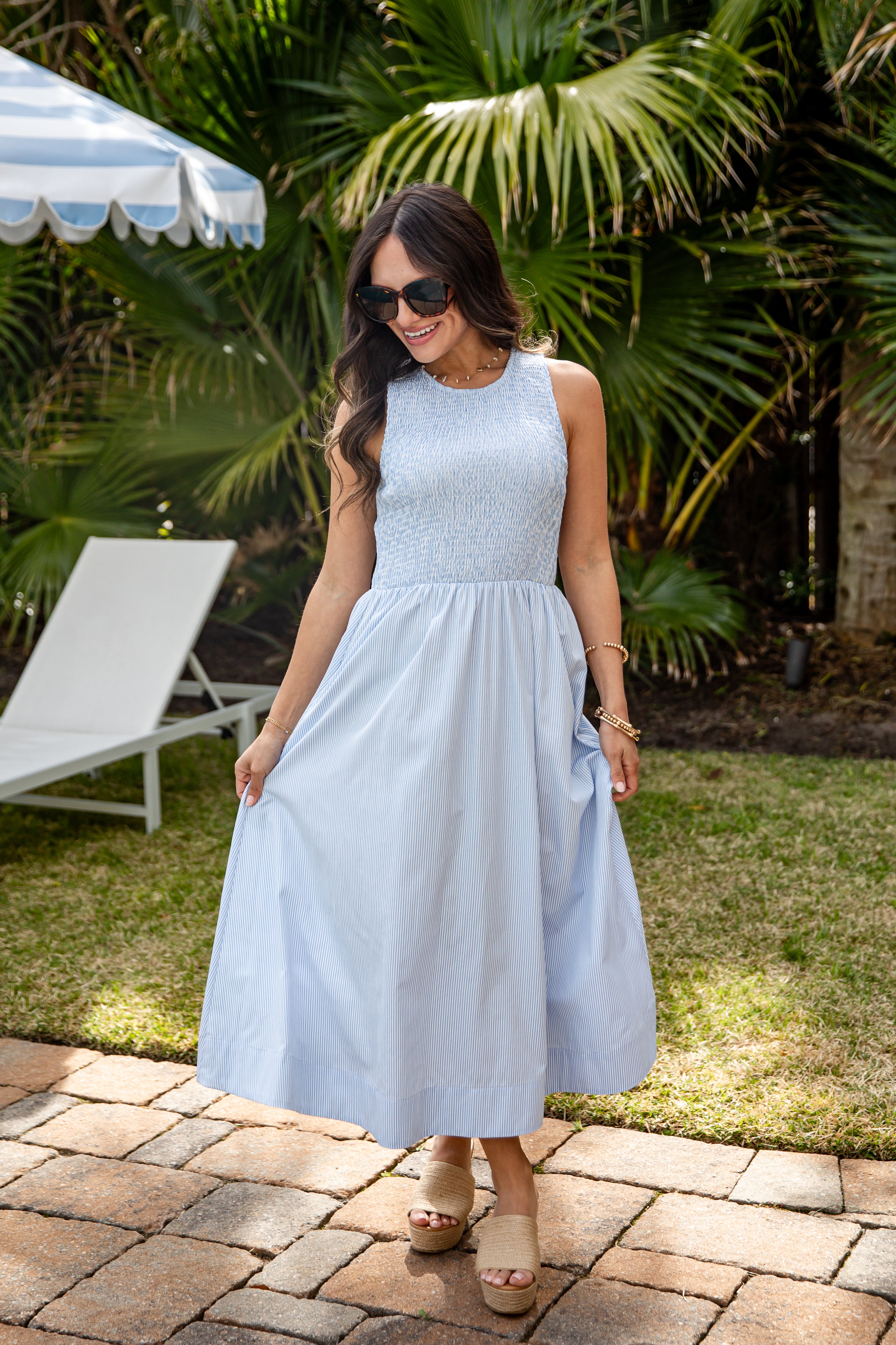 Woman in a light blue dress standing outdoors with palm trees in the background