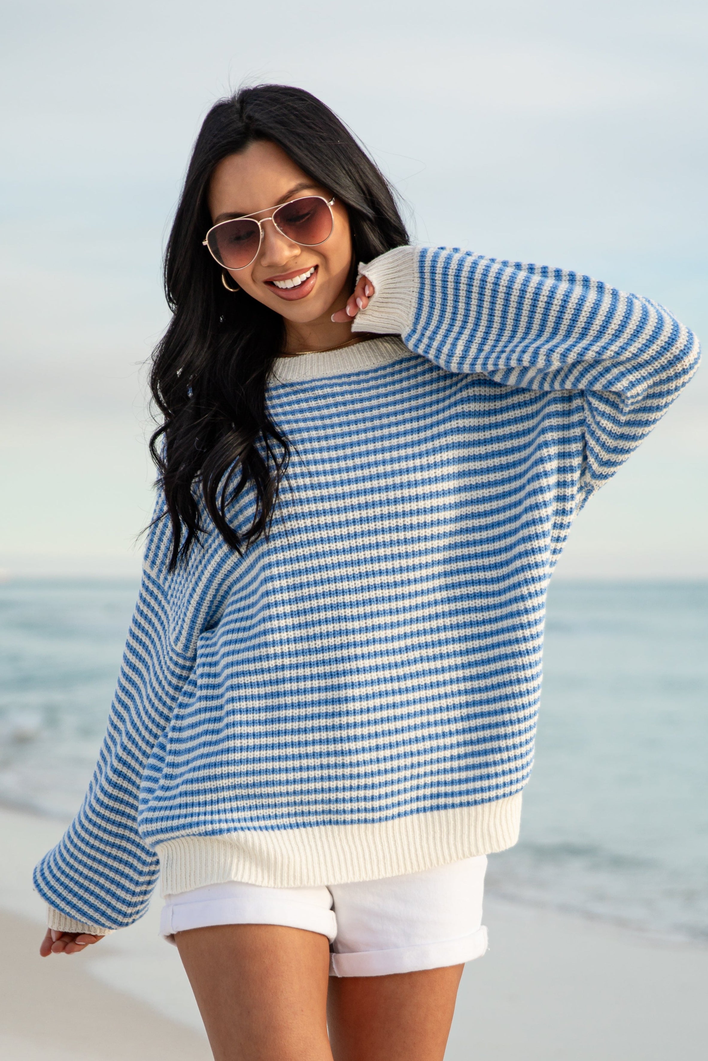 Woman wearing a blue and white striped sweater and white shorts on a beach.
