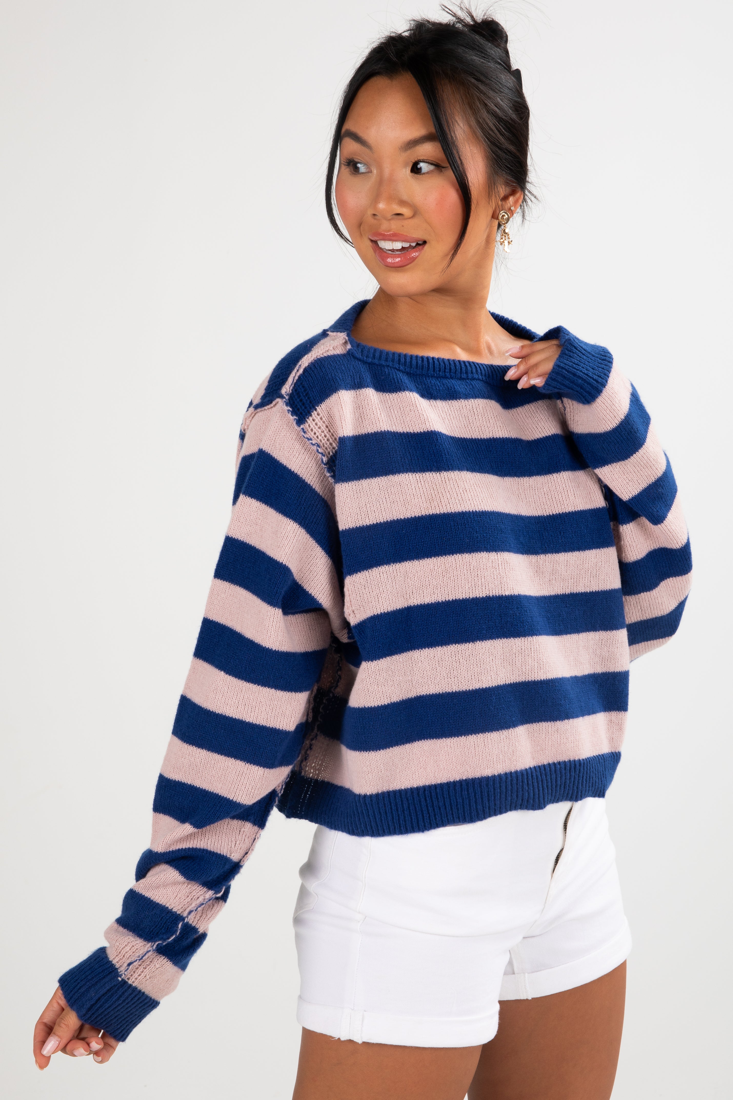 Woman wearing a blue and pink striped sweater with white shorts on a white background
