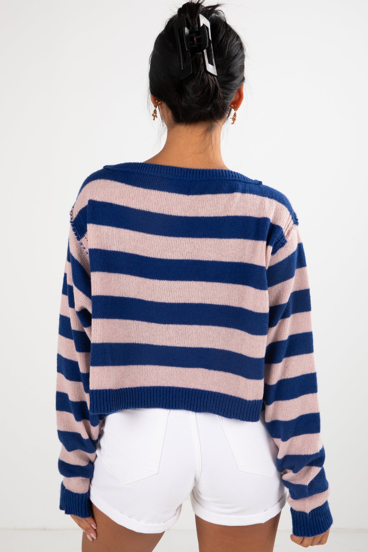 Person wearing a blue and pink striped sweater with white shorts on a plain background