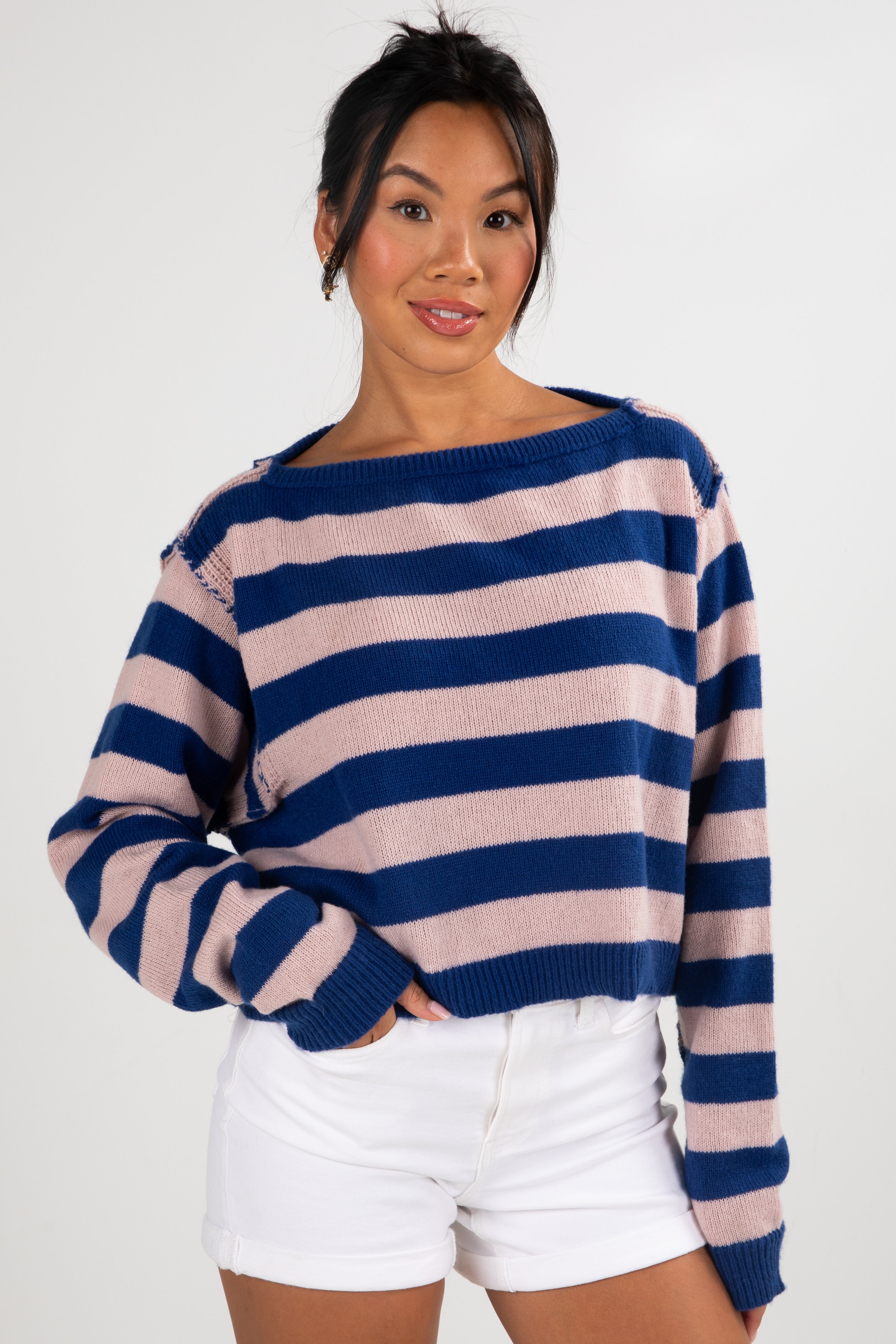 Woman wearing a blue and pink striped sweater with white shorts on a plain background