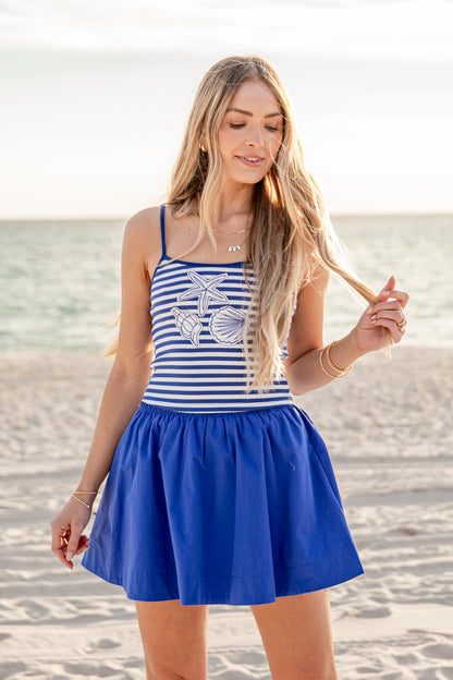 Woman in a blue and white striped dress with a blue skirt on a beach.