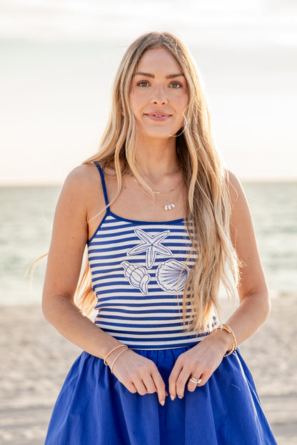 Woman wearing a blue and white striped tank top with starfish design on a beach.